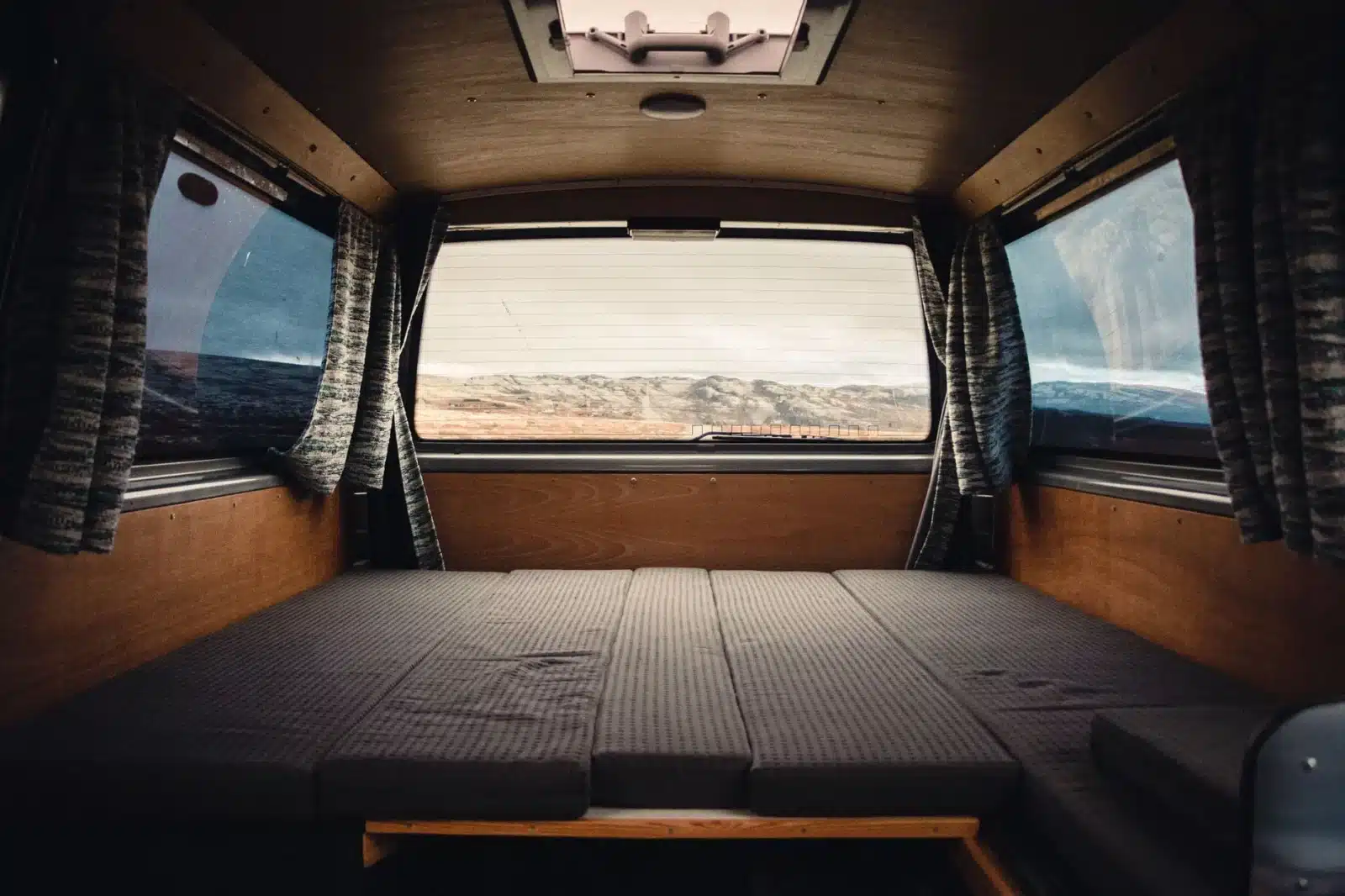 Intérieur d'un van aménagé avec cuisine fixe et banquette convertible en lit, prêt pour un road-trip
